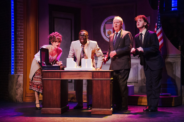 Production photo of Rock of Ages showing four actors gathered around a desk with shocked expressions.